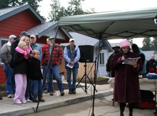 Habitat for Humanity of Kitsap County Executive Director Lori Oberlander (right) speaks to the large crowd gathered at Saturday's dedication ceremony at New Hope. The Natins family (left