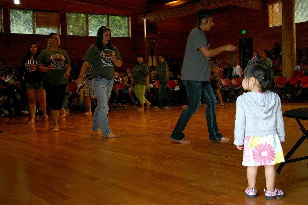 A girl watches Chehalis canoe family members as they dance to a paddle song in Suquamish's House of Awakened Culture July 21