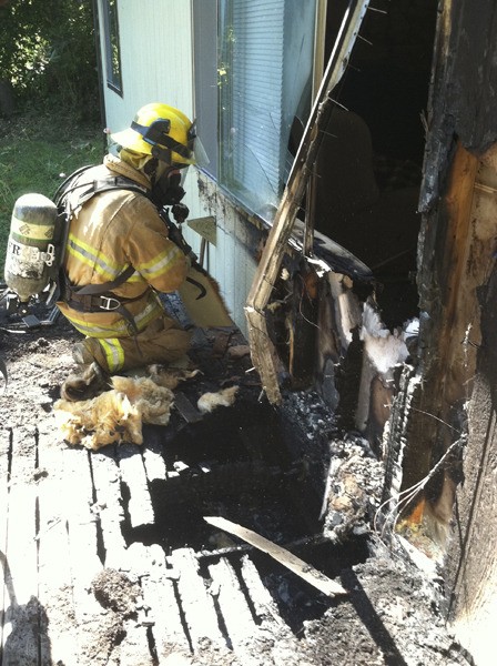 An NKF&R firefighter checks for extension of the fire by removing siding from a home that was scorched – most likely from a discarded cigarette — off of Miller Bay Road in Suquamish the afternoon of Aug. 30.