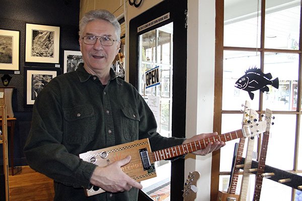 Terry Cott of Liberty Bay Gallery tries one of Ron Davison’s cigar box guitars. Liberty Bay Gallery