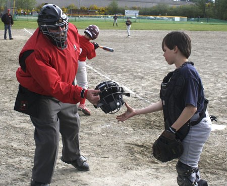 Longtime Bremerton umpire O.J. Simpson hands a catcher his mask during a Silverdale Pee Wee baseball game last week.