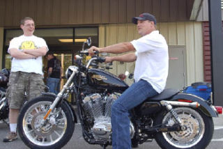 Klahowya Band Director Jeff McBirnie looks on as Shawn Varick sits on his new motorcycle outside Legend Harley-Davidson in Silverdale Tuesday. Varick was the winner in the band’s raffle.