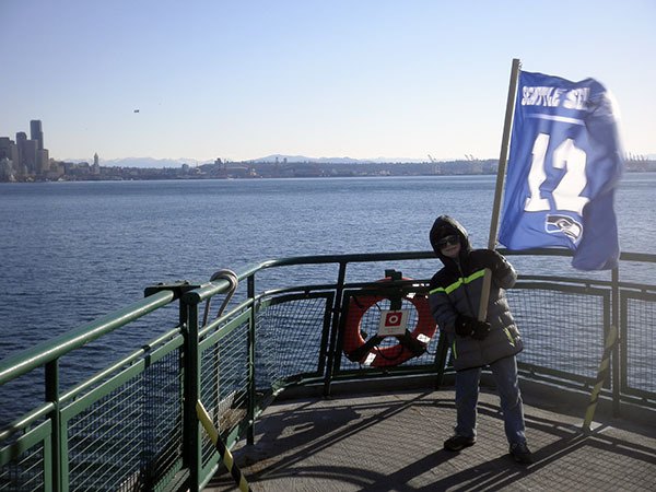 Alik Svardh of Hansville hoists the 12th Man flag on the ferry ride into Seattle for the Seahawks parade