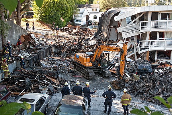 Firefighters watch as an excavator slowly moves through the rubble of the destroyed part of the Bremerton Motel 6 on Aug. 19.