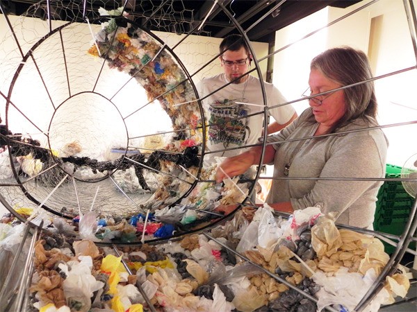 Theresa Helton and Max Greene weave plastic bags around the skeleton of the baby gray whale in The Gallery at Olympic College’s Bremerton campus. A show expressing the connection between humans and marine life will begin Oct. 4.