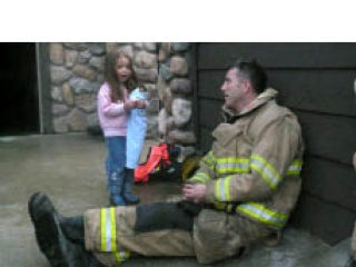 Central Kitsap Fire & Rescue firefighter Steve Davison visits with one of the three children whose house on NW El Camino Boulevard caught fire early Wednesday morning due to defective wiring.