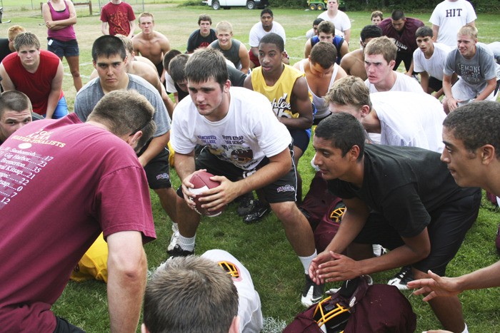 South Kitsap quarterback and co-captain Eddie Meisner holds the football as the Wolves gather around Coach D.J. Sigurdson (left