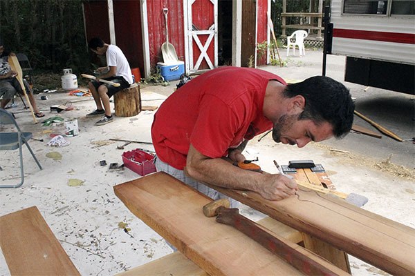 Sammy Mabe of the Sacred Water Canoe Family sketches a canoe on a slab of wood