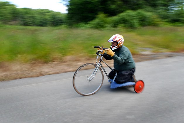 Hansville Coaster Games organizer Chuck Strahm speeds down Benchmark Avenue Monday on a homemade tricycle.