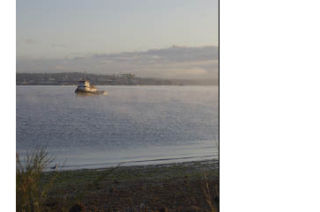 A boat sits on Puget Sound as fog eerily rolls past with Puget Sound Naval Shipyard as the backdrop.