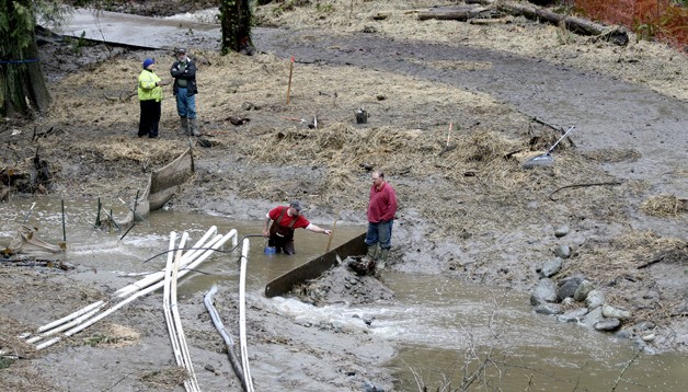 A crew works amid surging Lemolo Creek Sunday in a construction site off State Route 305.