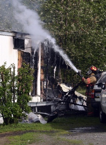 A firefighter douses a smoldering mobile home Wednesday off Scandia Road.