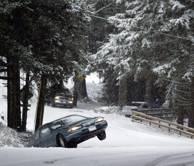 A stranded driver waits in his car as it sits in the ditch tilted above the ground on Tracyton Boulevard NW Thursday. More snow for the region is expected on Sunday.