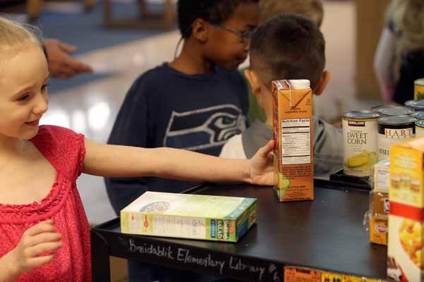 Breidablik Elementary Kindergartener Katie Casteel works on clearing the top shelf of a cart used to move boxed and canned food to the front entrance of the school. The food will be donated to North Kitsap Fishline in Poulsbo on Monday by interim principal Glen Robbins.