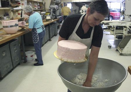 Debbie Crowl sprinkles coconut on the side of a pink champagne cake at McGavin's Bakery Tuesday.